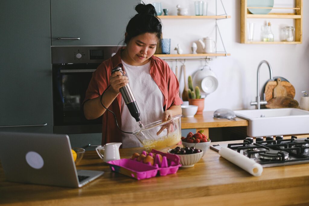 Woman using a mixer in a modern kitchen, preparing food with fresh ingredients.