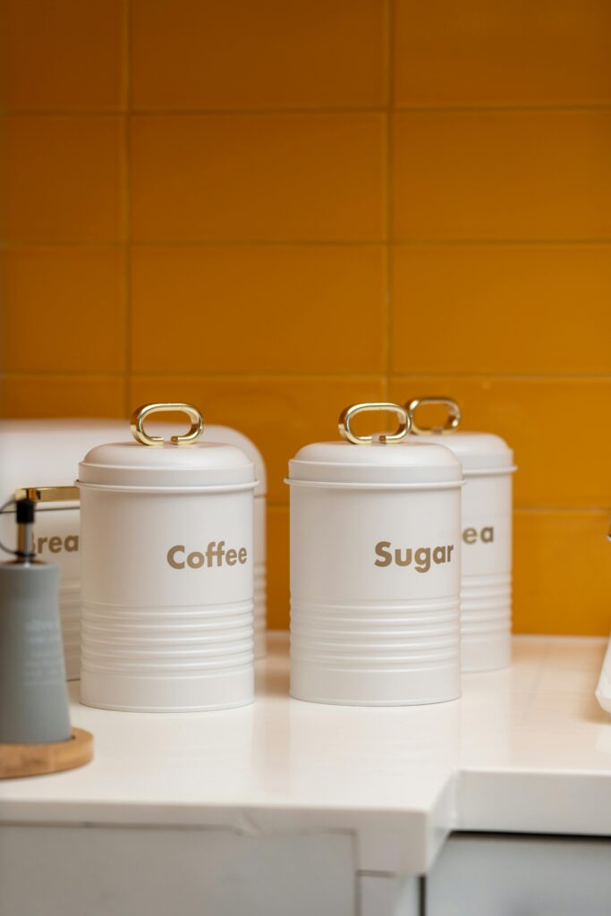 Elegant white kitchen canisters labeled for coffee and sugar, against a vibrant yellow backsplash.